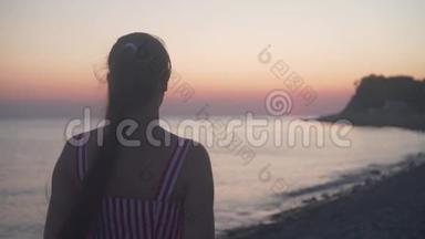 一个年轻的女孩<strong>站在</strong>海<strong>上</strong>日落的背景<strong>上</strong>。 一个女人背对着镜头<strong>站在海滩上</strong>。
